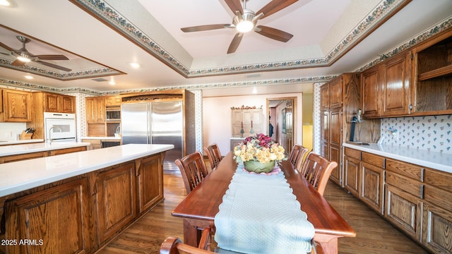 dining area featuring dark wood-type flooring, a raised ceiling, ceiling fan, and sink