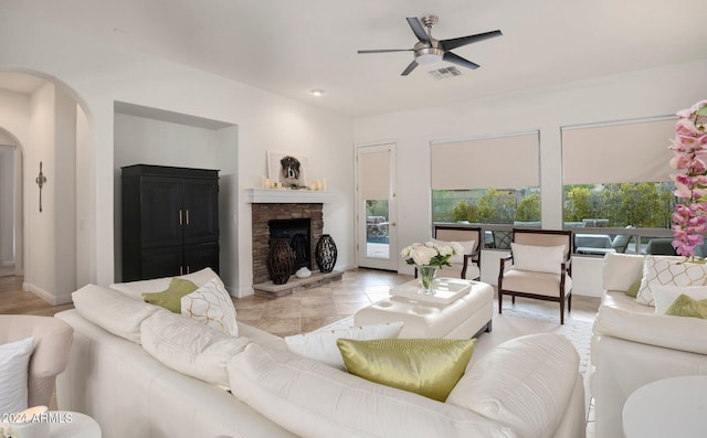 living room with visible vents, a ceiling fan, arched walkways, a fireplace, and light tile patterned floors