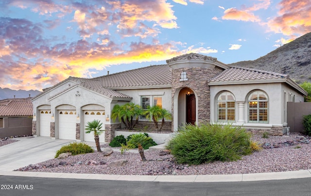 mediterranean / spanish-style home featuring a garage, stone siding, and stucco siding