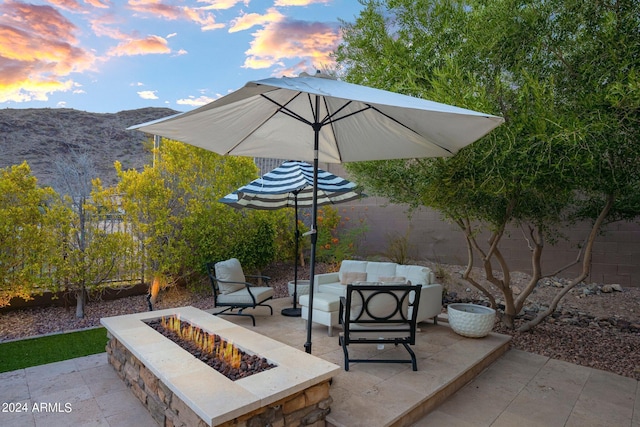 patio terrace at dusk featuring a mountain view, an outdoor living space with a fire pit, and fence