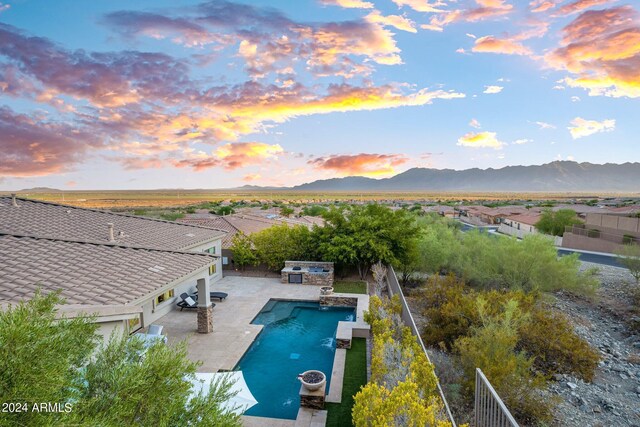 pool at dusk with a fenced in pool, a fenced backyard, a mountain view, and an outdoor kitchen