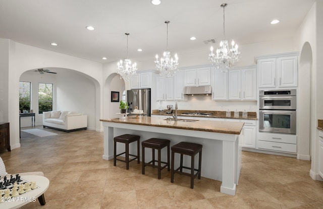 kitchen with visible vents, under cabinet range hood, arched walkways, stainless steel appliances, and a sink