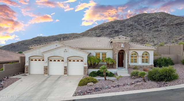 mediterranean / spanish home featuring stone siding, stucco siding, an attached garage, and fence