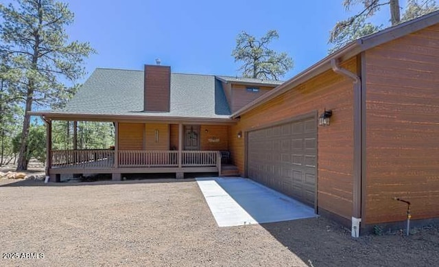 view of front facade with a garage, driveway, a chimney, and covered porch