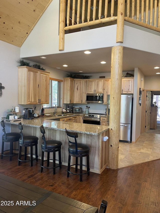 kitchen featuring light stone counters, a peninsula, appliances with stainless steel finishes, and light brown cabinets