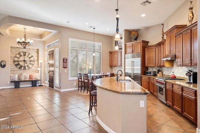 kitchen with sink, a center island with sink, hanging light fixtures, and premium appliances