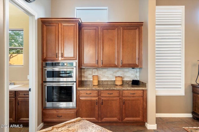 kitchen with tasteful backsplash, light stone countertops, and stainless steel double oven