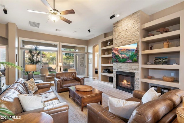 living room with a fireplace, ceiling fan, built in features, and light hardwood / wood-style flooring