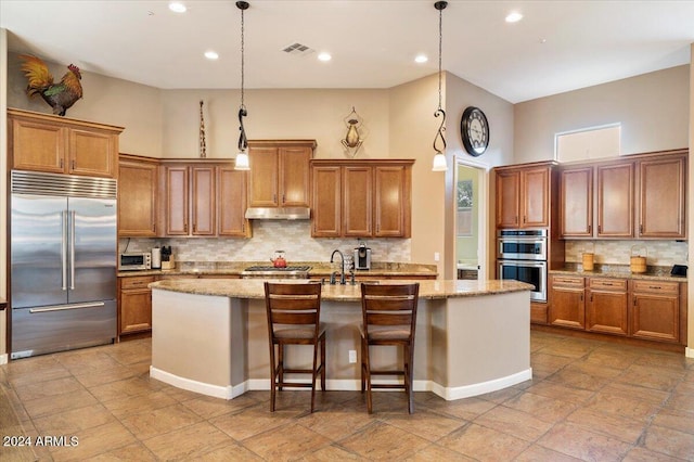 kitchen featuring stainless steel appliances, hanging light fixtures, and an island with sink