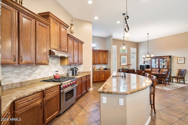 kitchen with stainless steel range, sink, hanging light fixtures, decorative backsplash, and a center island with sink