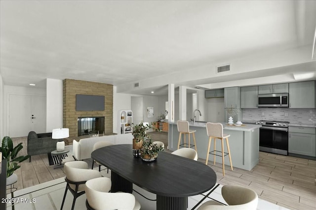 dining area featuring a brick fireplace, visible vents, and light wood-style flooring