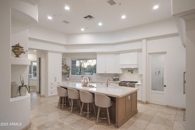 kitchen featuring a kitchen bar, sink, a center island with sink, light stone countertops, and white cabinets