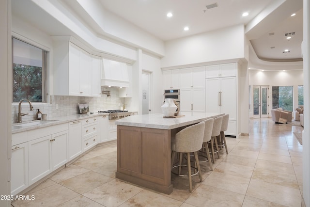 kitchen with tasteful backsplash, white cabinetry, sink, custom exhaust hood, and a center island