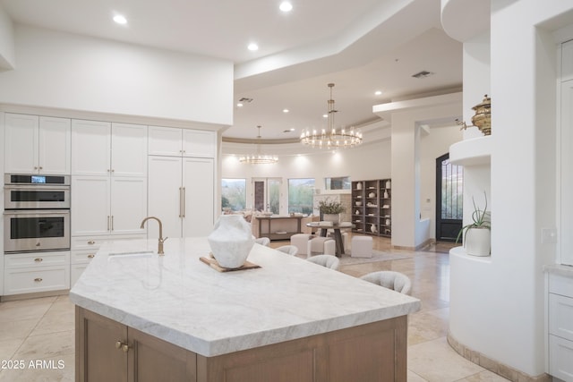 kitchen with a large island, pendant lighting, sink, white cabinetry, and double oven