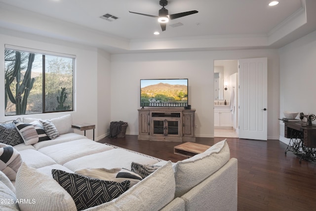 living room featuring a raised ceiling, ornamental molding, dark wood-type flooring, and ceiling fan