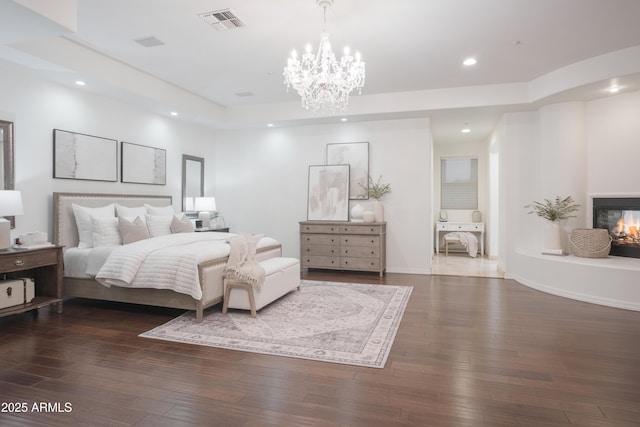 bedroom with a multi sided fireplace, dark hardwood / wood-style flooring, a raised ceiling, and a notable chandelier