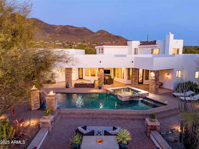 pool at dusk featuring an in ground hot tub, a mountain view, and a patio