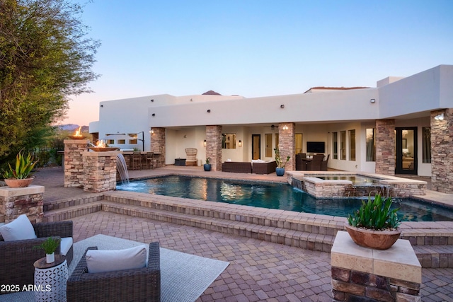 pool at dusk featuring pool water feature, area for grilling, an outdoor bar, an in ground hot tub, and a patio