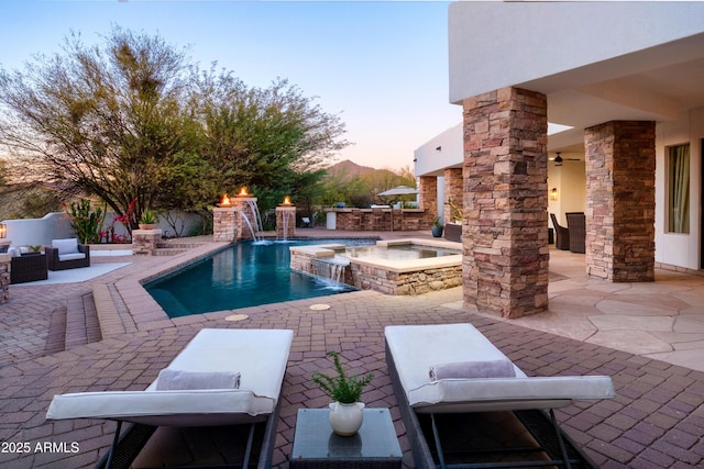 pool at dusk with an in ground hot tub, pool water feature, and a patio area