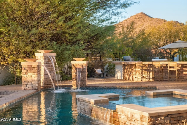 view of swimming pool with an outdoor hot tub, a mountain view, an outdoor bar, and pool water feature