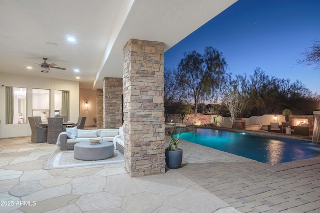 pool at dusk featuring pool water feature, ceiling fan, outdoor lounge area, and a patio