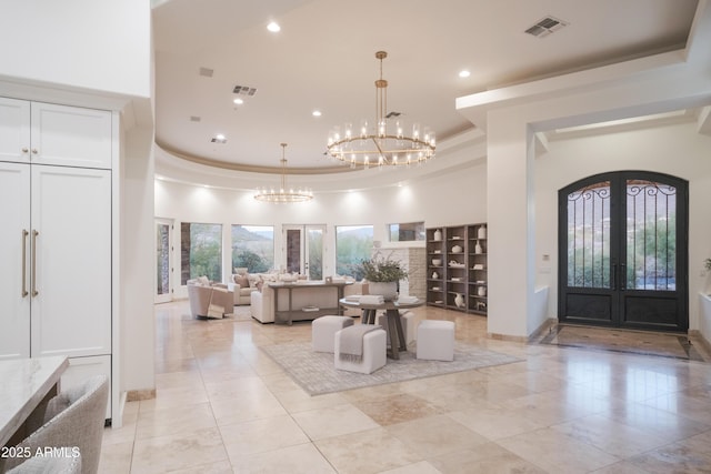 entrance foyer with french doors, crown molding, a chandelier, a raised ceiling, and a towering ceiling