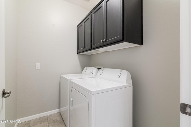 clothes washing area with cabinets, light tile patterned floors, and washer and clothes dryer