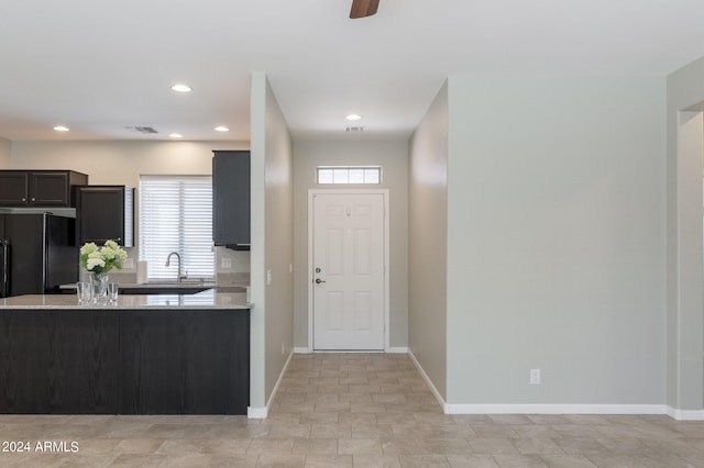 kitchen featuring light stone counters, black fridge, sink, and ceiling fan