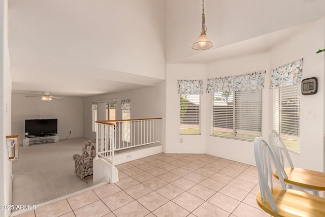 unfurnished dining area with healthy amount of natural light, ceiling fan, light tile patterned floors, and a towering ceiling