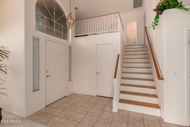 foyer with stairway, light tile patterned floors, and a towering ceiling