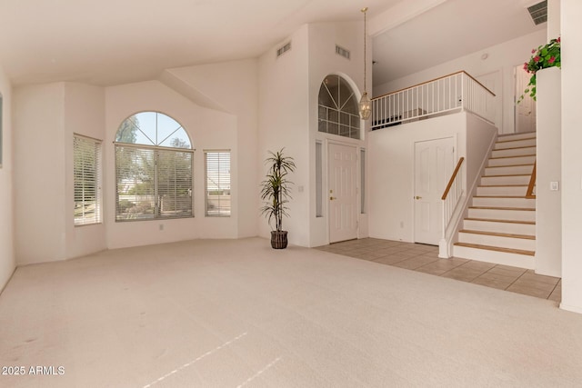 unfurnished living room with carpet flooring, high vaulted ceiling, stairs, and tile patterned floors