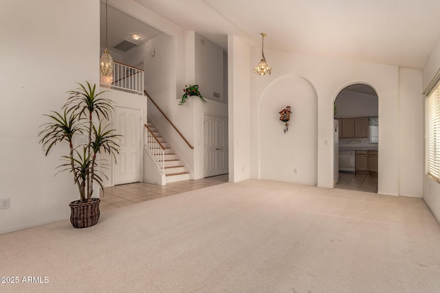 unfurnished living room with carpet floors, arched walkways, stairs, and vaulted ceiling