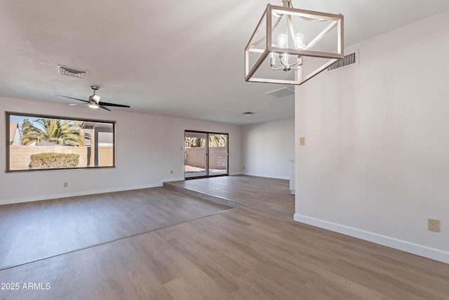 empty room featuring ceiling fan with notable chandelier and hardwood / wood-style floors