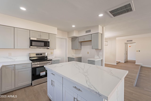 kitchen featuring a center island, gray cabinets, light hardwood / wood-style floors, light stone countertops, and appliances with stainless steel finishes