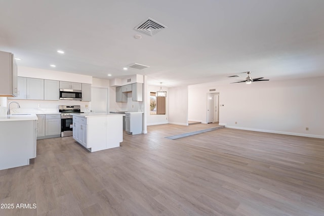 kitchen featuring stainless steel appliances, a center island, ceiling fan, sink, and light hardwood / wood-style flooring