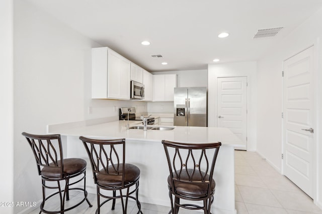 kitchen featuring light tile patterned flooring, a breakfast bar area, kitchen peninsula, stainless steel appliances, and white cabinets