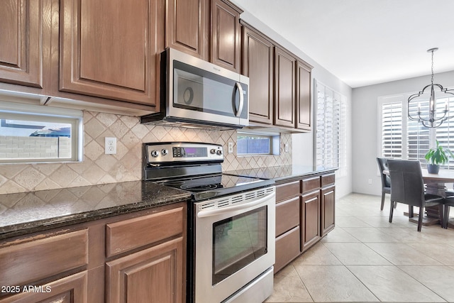 kitchen featuring tasteful backsplash, dark stone countertops, hanging light fixtures, light tile patterned floors, and stainless steel appliances