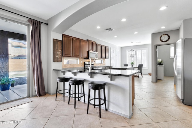 kitchen with appliances with stainless steel finishes, backsplash, a kitchen bar, decorative light fixtures, and kitchen peninsula