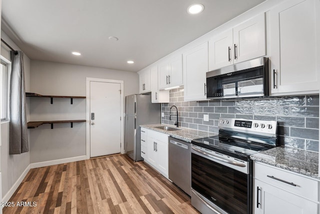 kitchen with stainless steel appliances, light stone counters, sink, light hardwood / wood-style flooring, and white cabinetry