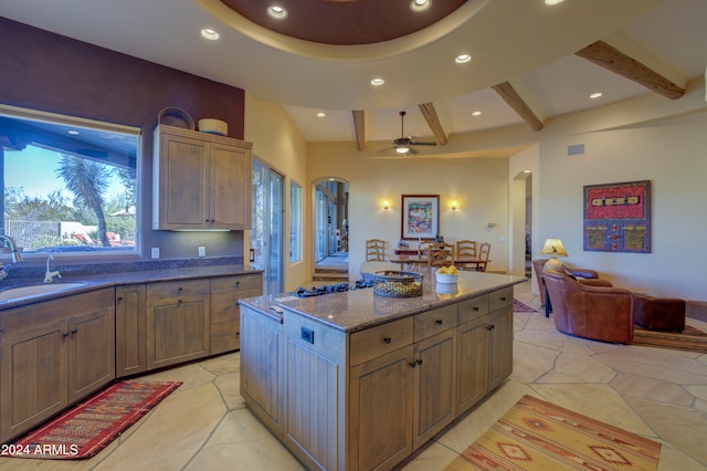 kitchen with dark stone counters, sink, ceiling fan, a kitchen island, and beam ceiling