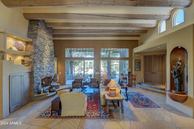 living room featuring beam ceiling, a stone fireplace, and a towering ceiling