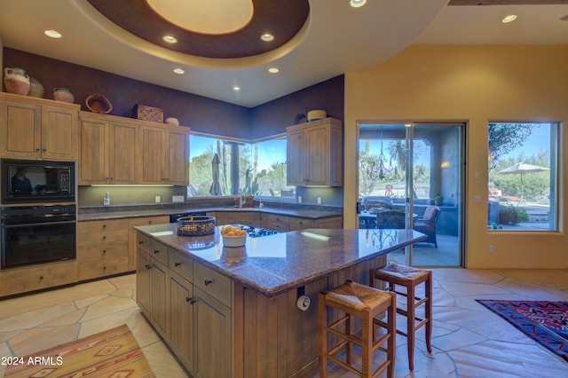 kitchen featuring a breakfast bar, a high ceiling, dark stone counters, black appliances, and a kitchen island