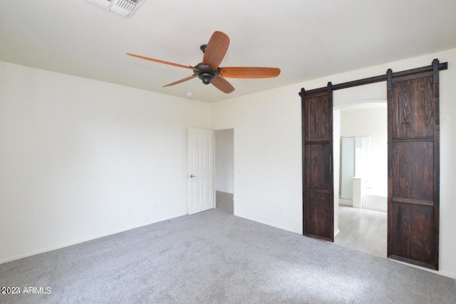 unfurnished bedroom featuring a barn door, ceiling fan, and light carpet