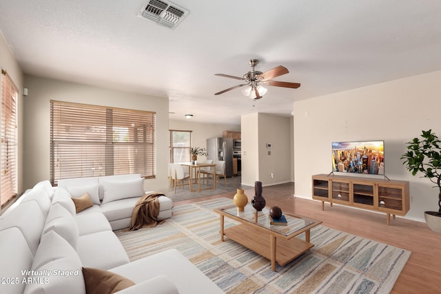 living area with a ceiling fan, light wood-style flooring, and baseboards