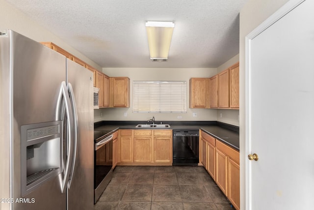 kitchen with appliances with stainless steel finishes, a sink, dark countertops, a textured ceiling, and dark tile patterned flooring