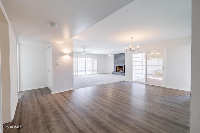 unfurnished living room featuring a fireplace, dark wood-type flooring, and ceiling fan with notable chandelier