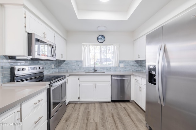 kitchen with appliances with stainless steel finishes, tasteful backsplash, sink, white cabinets, and a tray ceiling