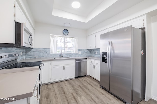 kitchen with a tray ceiling, white cabinets, appliances with stainless steel finishes, and sink