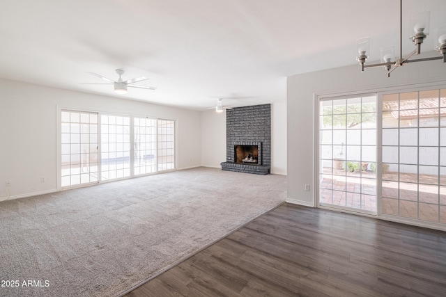 unfurnished living room with ceiling fan with notable chandelier, dark hardwood / wood-style floors, and a fireplace