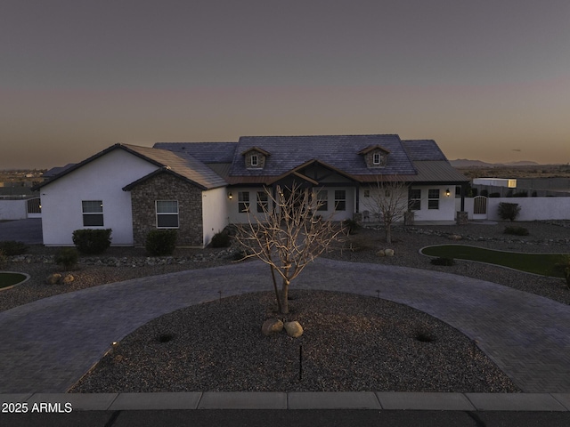 french country home featuring decorative driveway, stone siding, and stucco siding